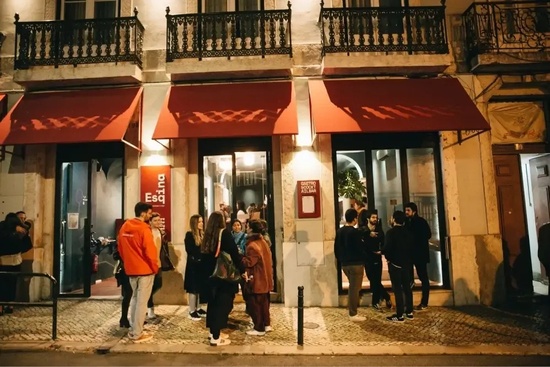 un grupo de personas se paran frente a un edificio con una puerta roja que dice esq.ina