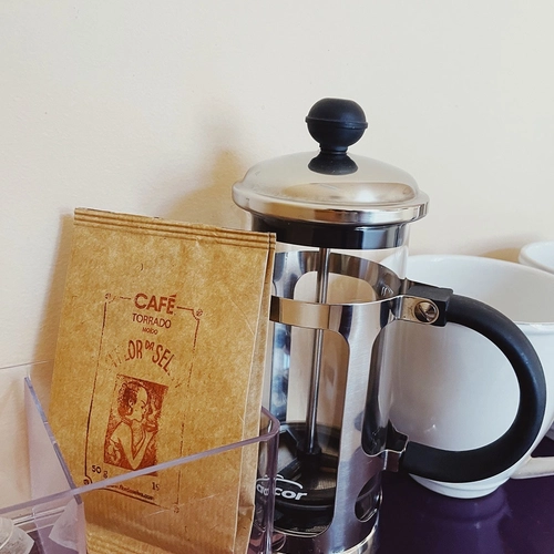 a bag of cafe torrado sits next to a french press