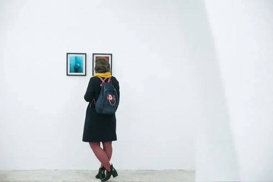 a woman with a backpack is looking at pictures on a wall