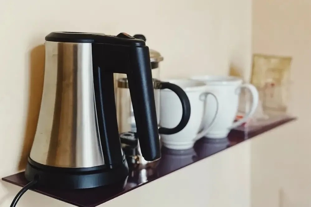 a stainless steel kettle sits on a shelf next to cups