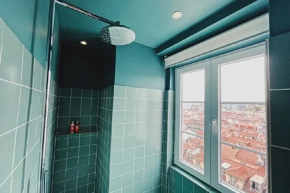 a bathroom with green tiles and a window with a view of a city