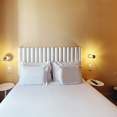 a bed with white sheets and pillows in a hotel room
