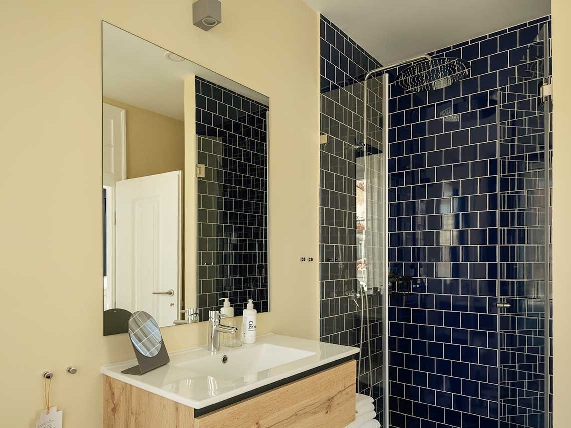 Un cuarto de baño moderno con paredes amarillo pálido, un lavabo sobre un mueble de madera, un gran espejo y una ducha con azulejos azul marino.
