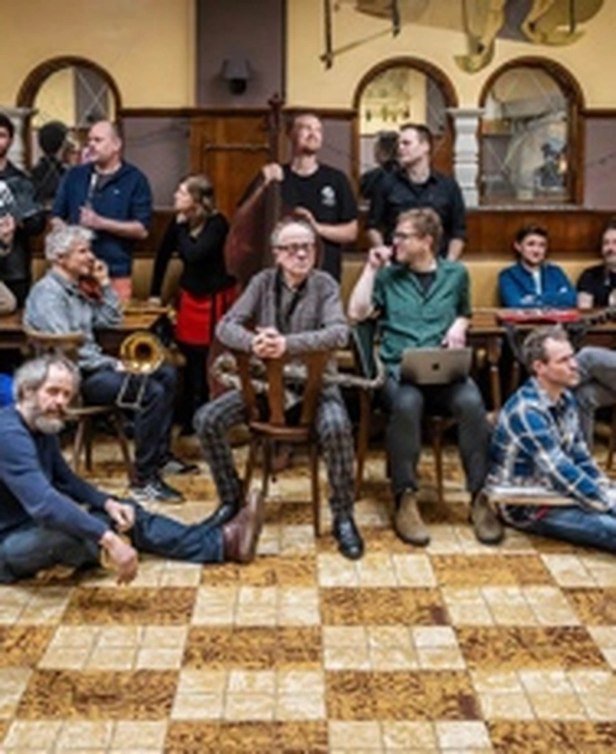 Group of musicians sitting in a room with a checkered floor.