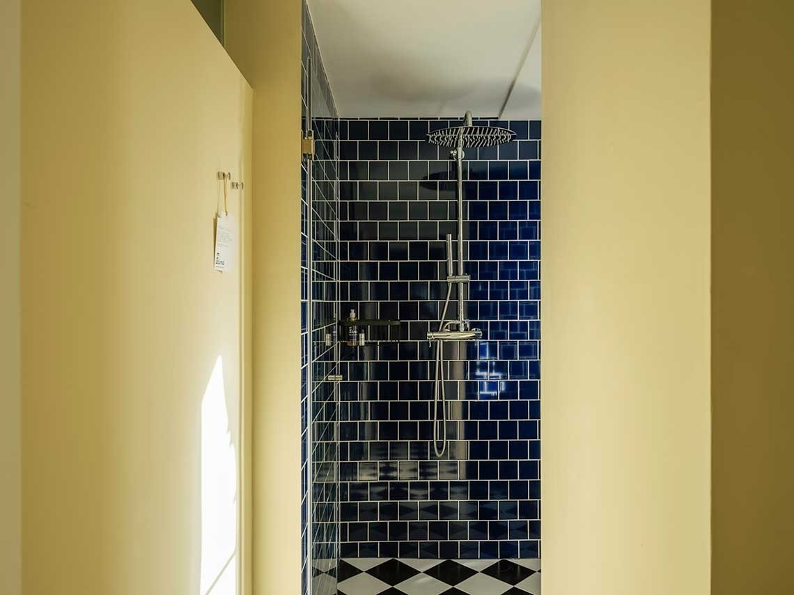 Un pasillo con paredes de color crema conduce a una moderna ducha con azulejos azul marino y un suelo de rombos en blanco y negro.