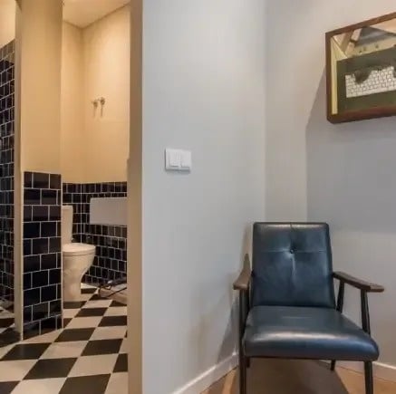 uma cadeira está sentada no canto de uma sala ao lado de um banheiro .