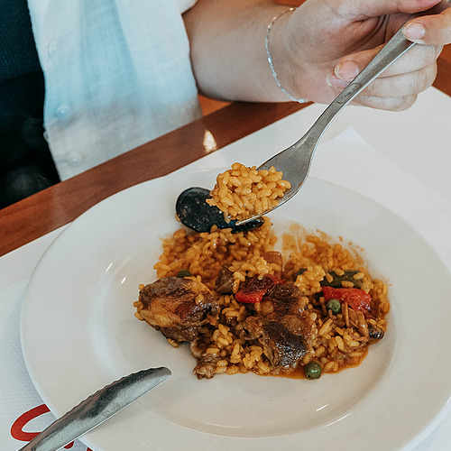 Person eating paella from a white plate with a fork, a delicious ESTIVAL: D Altafulla meal.