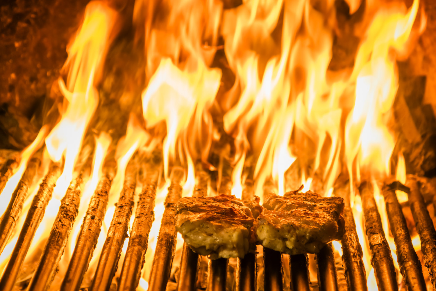 Calcots asándose a la parrilla sobre brasas ardientes, con humo y llamas visibles.