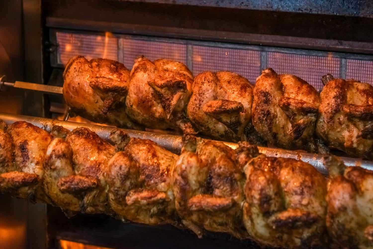 Calcots asándose a la parrilla sobre brasas ardientes, con humo y llamas visibles.