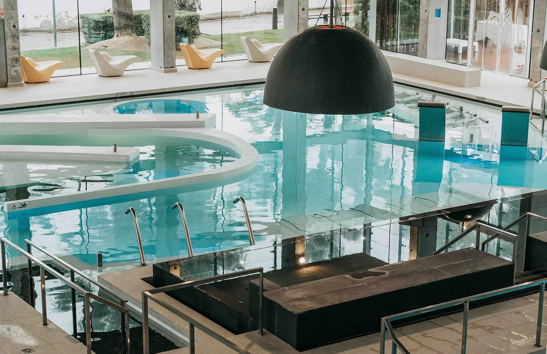 ESTIVAL: Aquum Spa, piscina interior con tumbonas y diseño moderno.