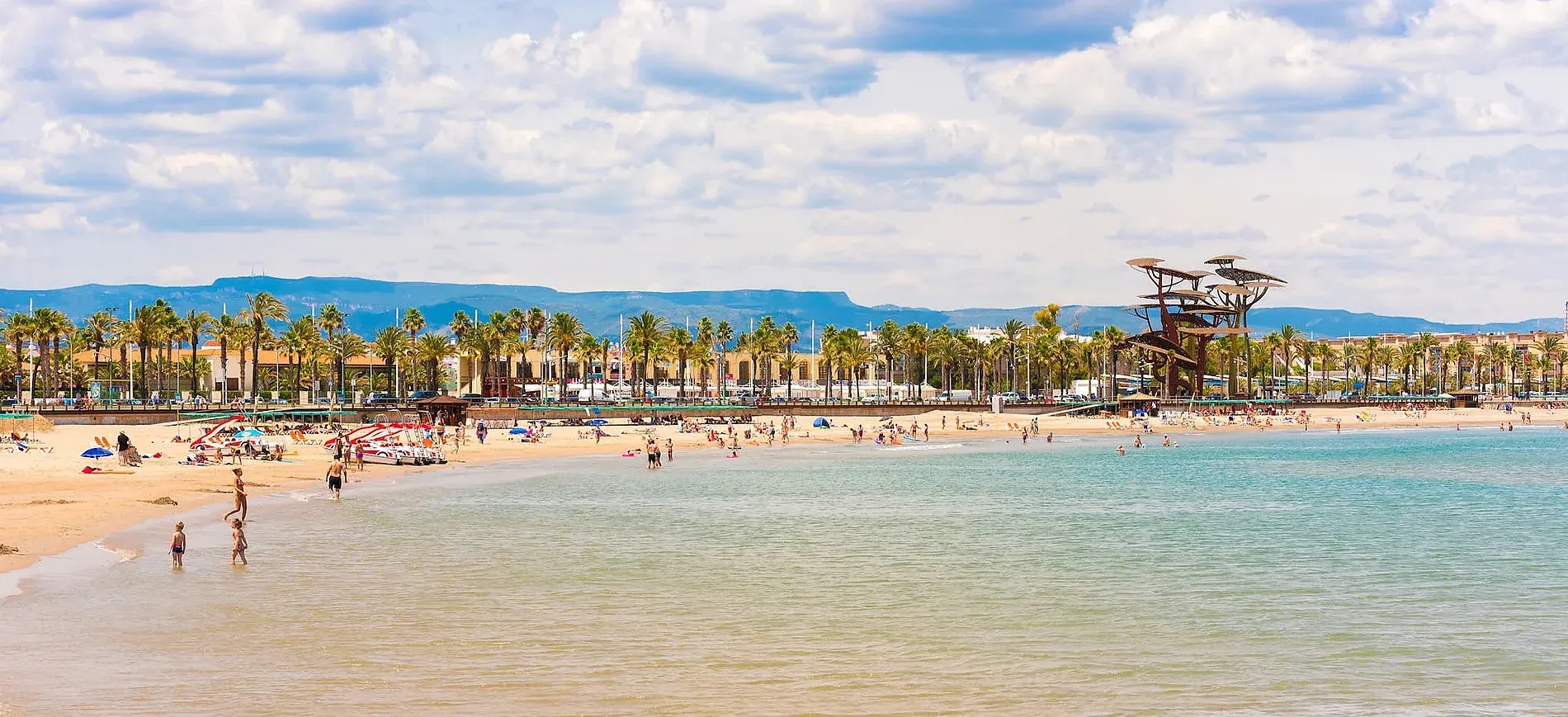 Playa soleada con palmeras, gente disfrutando del mar y el sol. Contacto y Localización | Aquum Spa & Wellness | Web Oficial