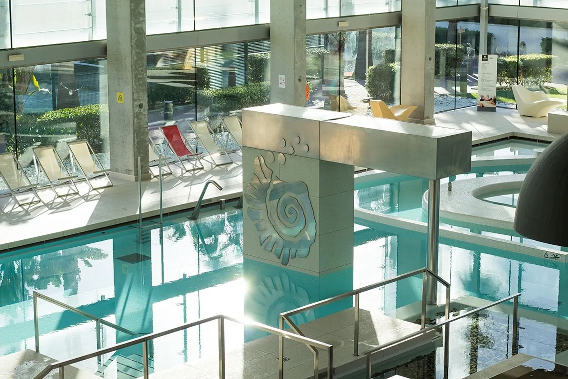 Piscina interior de ESTIVAL: Oassium Hotel con tumbonas y decoración espiral.