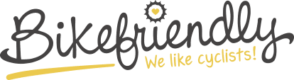 Un logo con la palabra "Bikefriendly" en tipografía cursiva, acompañado de un engranaje con un corazón y el lema "We like cyclists!", todo en tonos grises y amarillos sobre un fondo negro.