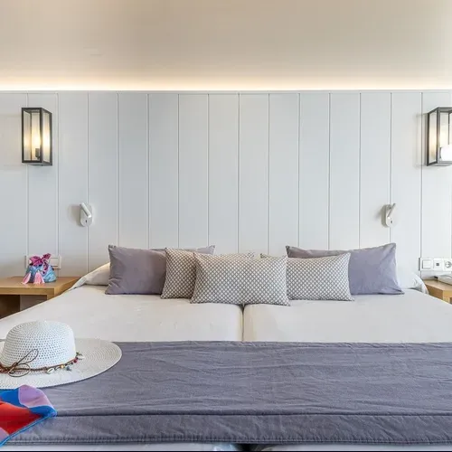 Estival Torrequebrada: White bed with pillows, hat, and colorful scarf. Estival Group.