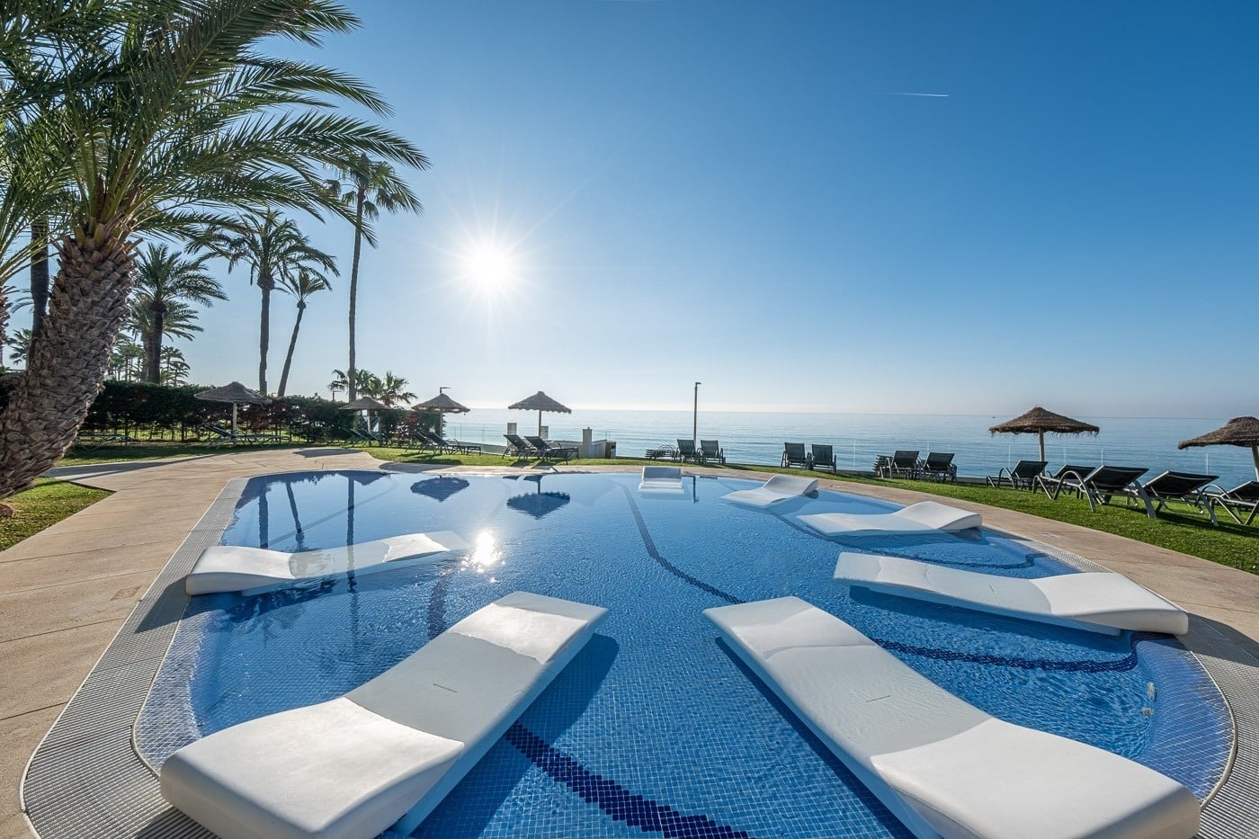 Piscina de lujo en Estival Torrequebrada Benalmádena, con tumbonas y vistas al mar.