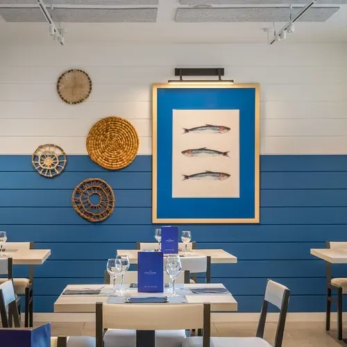 Interior of a restaurant at ESTIVAL: Corporativa, featuring tables set with white chairs and a blue and white striped wall.