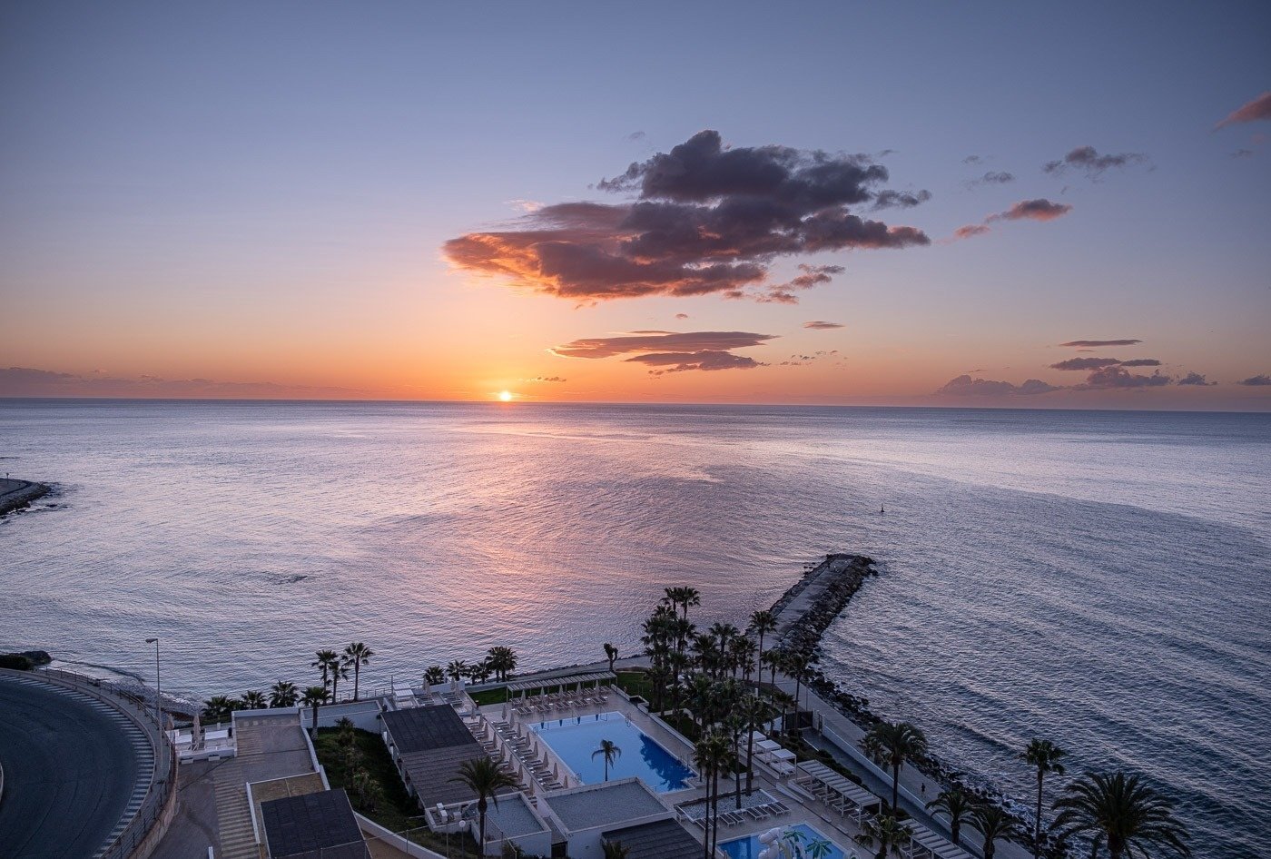 a sunset over the ocean with a swimming pool in the foreground