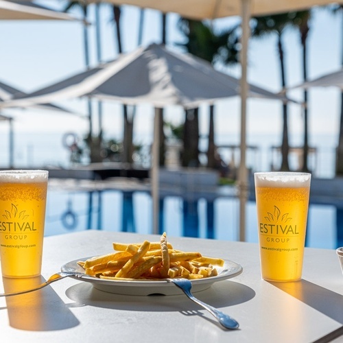 a plate of french fries sits on a table next to two glasses of festival group beer