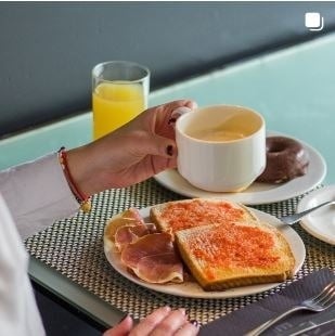 Eine Person hält eine Tasse Kaffee neben einem Teller mit Toast , Schinken und Donuts .