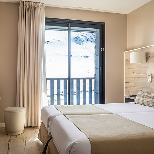 Cozy hotel room with a bed, balcony view of snowy mountains, and lamp. ESTIVAL: Corporativa