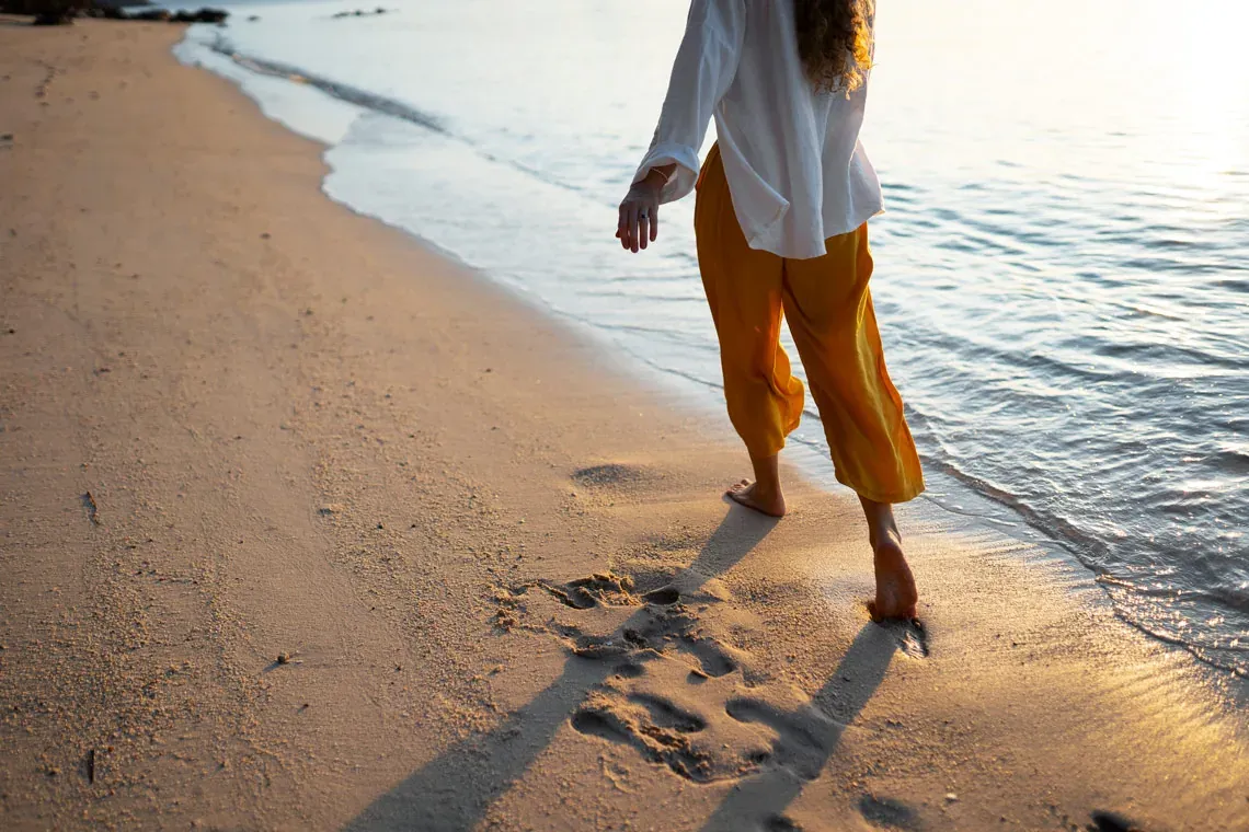ESTIVAL: Corporativa: Mujer paseando descalza por la playa al atardecer.
