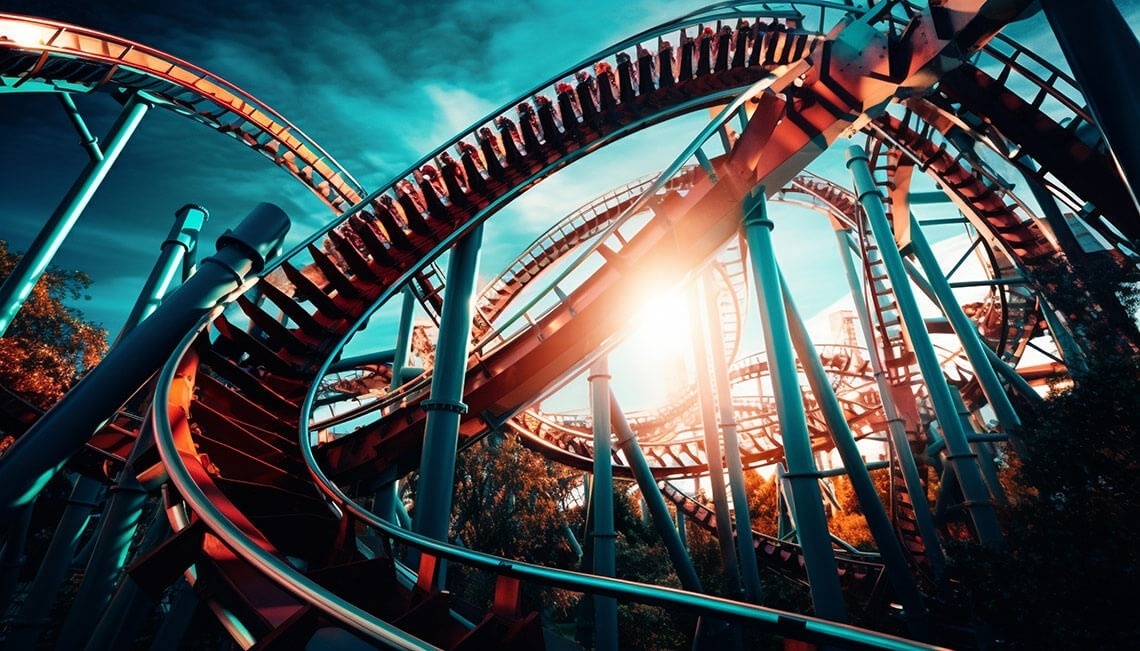 una montaña rusa en un parque de diversiones con el sol brillando a través de los árboles