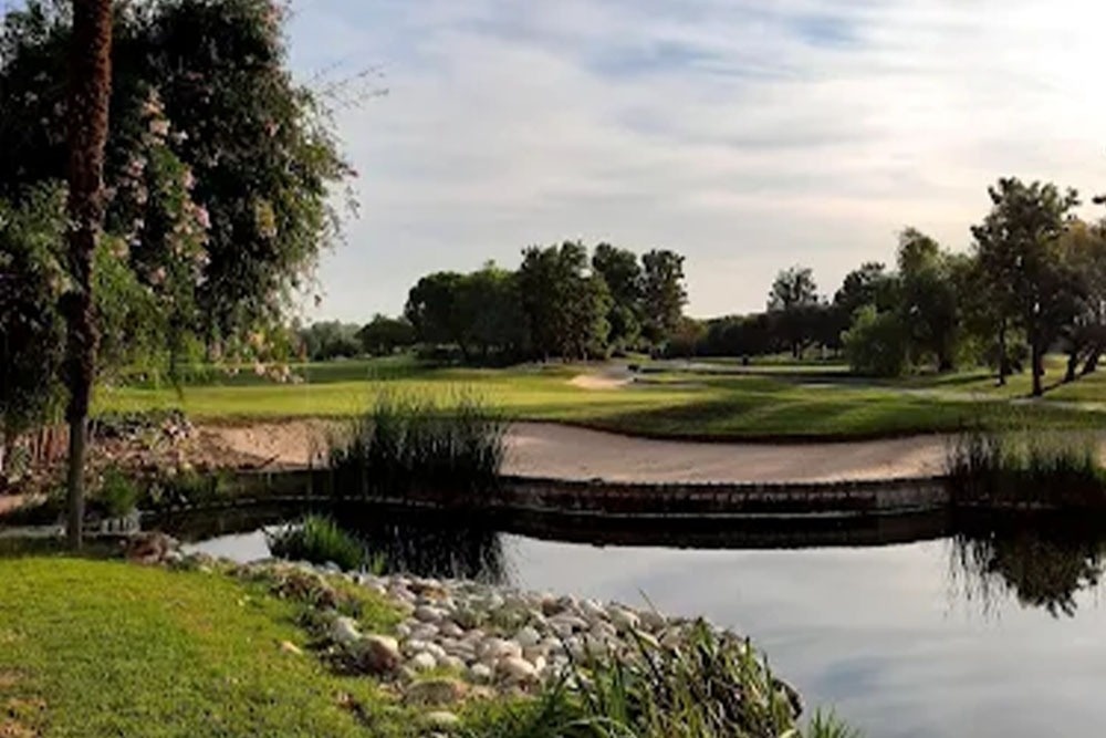 Ein Mann und eine Frau gehen mit ihren Golfausrüstungen über einen grünen Golfplatz, mit Bäumen im Hintergrund.