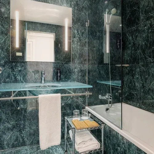 Modern bathroom with green marble, glass vanity, and bathtub at Hotel Vilamari Barcelona | Estival Group.