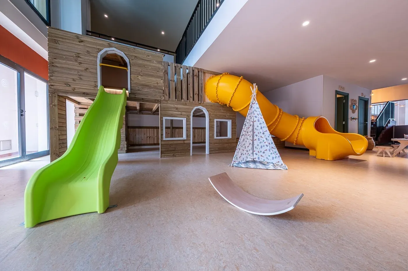 ESTIVAL Children's play area: yellow and green slides, wooden playhouse.