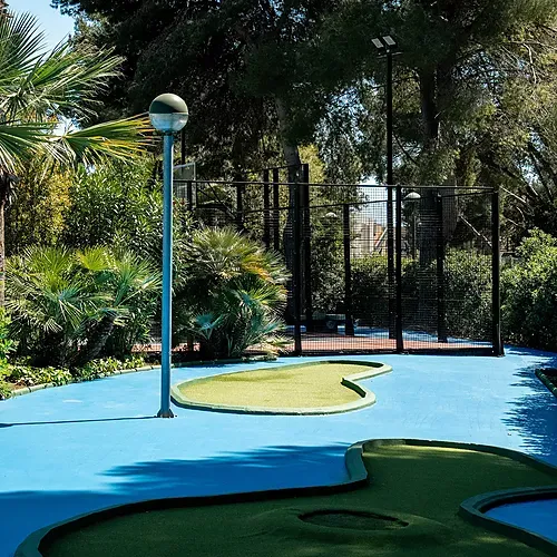 Mini-golf extérieur sur fond bleu, palmiers et terrain de paddle, à l'Estival Torre de la Mora, Tarragone.