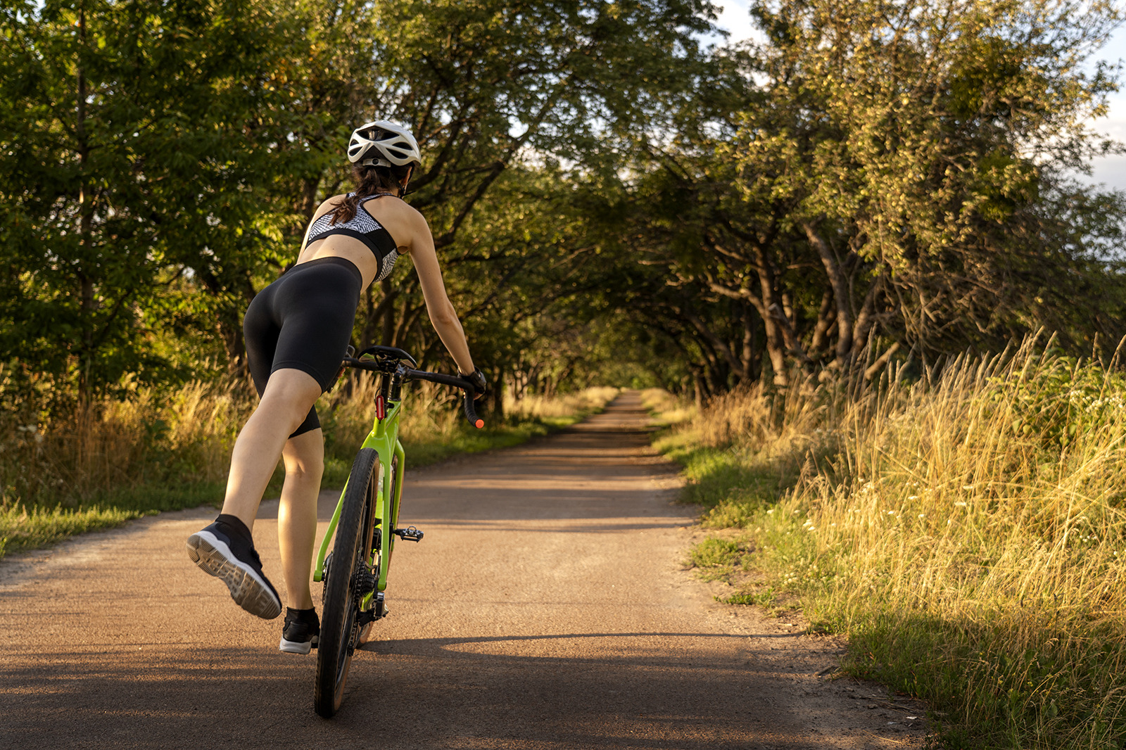 Femme cycliste sur route bordée d'arbres, parfaite pour votre séjour à l'hôtel. ESTIVAL: Corporativa
