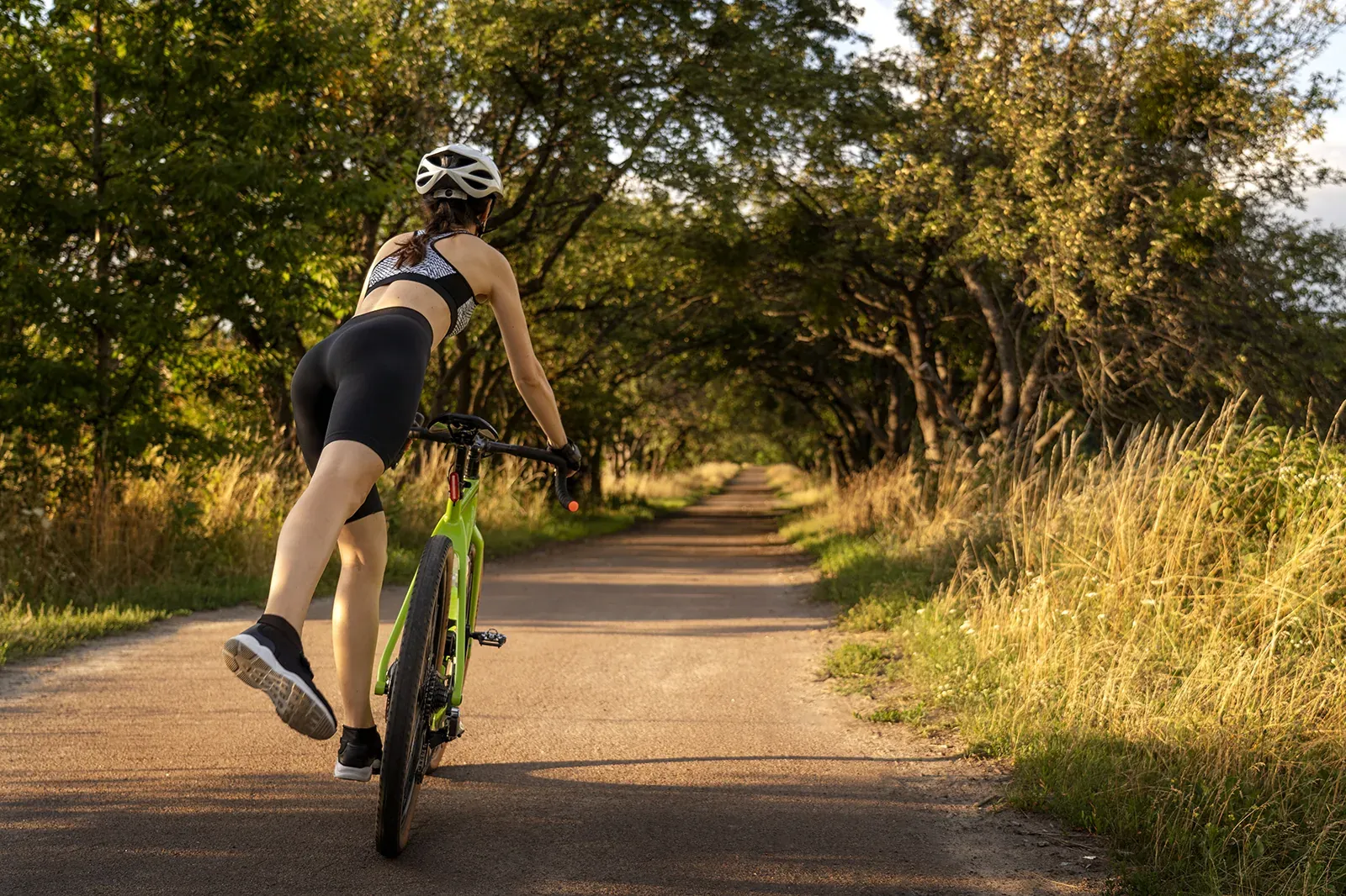 Frau auf Fahrrad auf einem Weg unter Bäumen, perfekt für einen Aufenthalt im Hotel ESTIVAL: Corporativa.