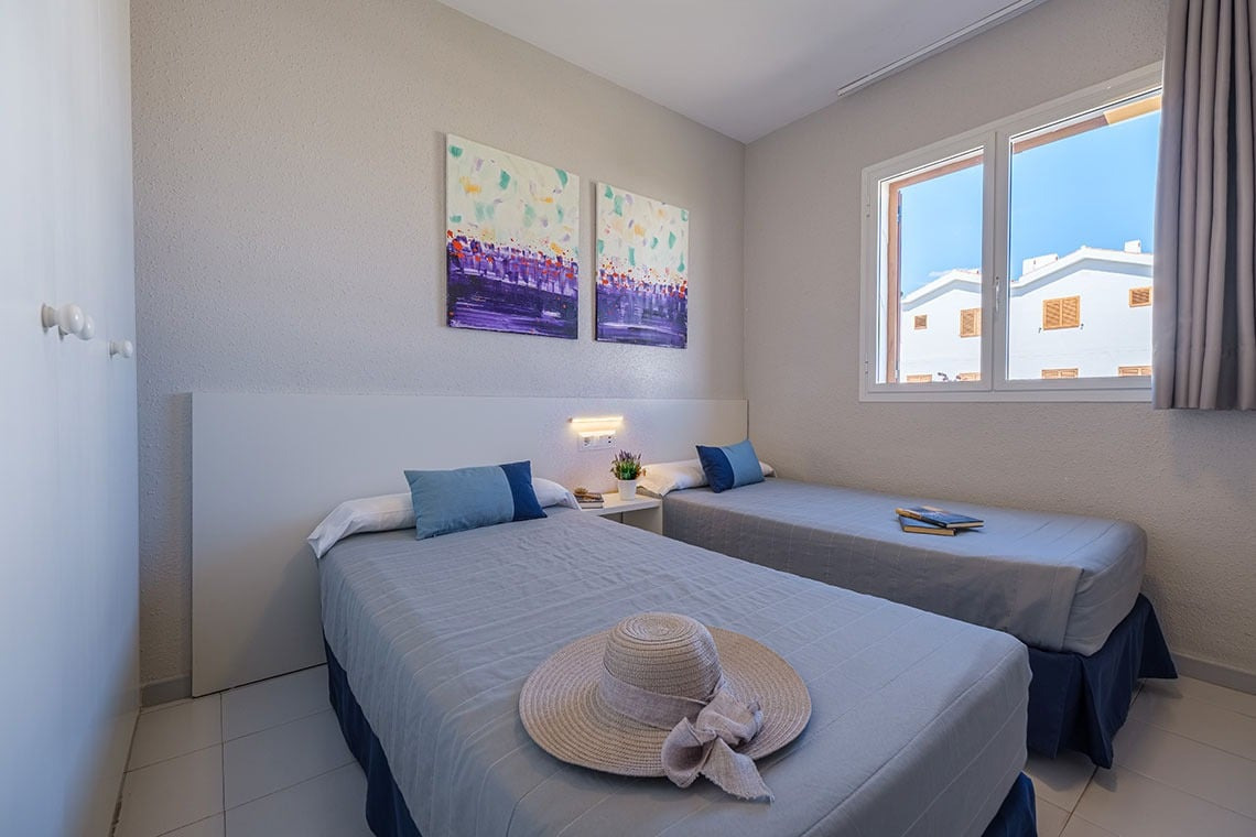 Gemütliches Doppelzimmer mit zwei Einzelbetten, Kunst an der Wand und Blick auf weiße Häuser. ESTIVAL: Corporativa