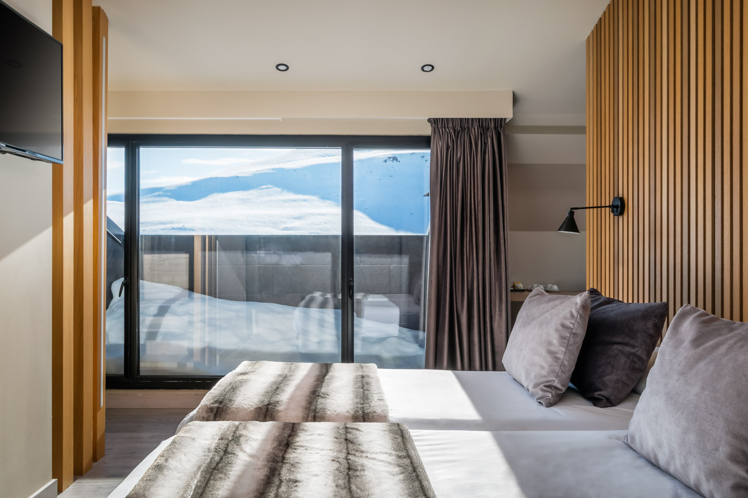Gallery | Hotel Caribou Andorra | Estival Group | Official Web - Twin beds in a modern hotel room with bedside lamps and balcony view.
