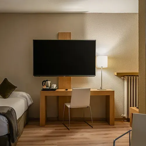 Modern hotel room with single bed, desk, TV & helmets. Hotel Sporting Andorra | Grandvalira Pas de la Casa.