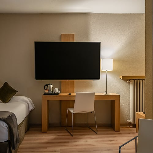 Modern hotel room with single bed, desk, TV & helmets. Hotel Sporting Andorra | Grandvalira Pas de la Casa.