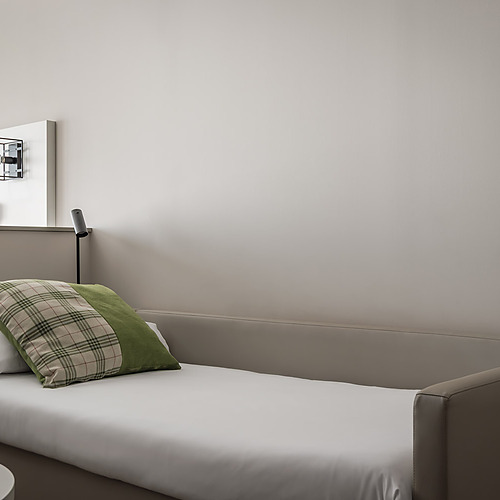 Sofá cama confortable en habitación de hotel con almohadas a cuadros y verde. ESTIVAL: Corporativa