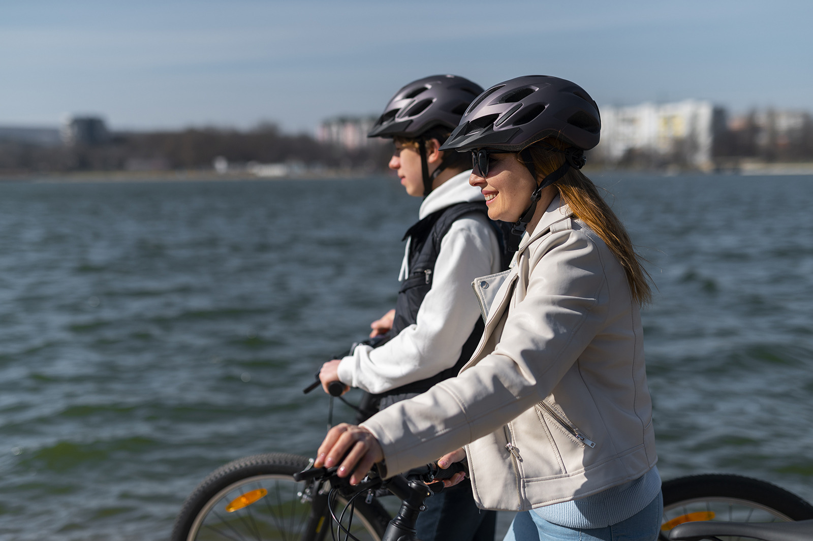 Couple à vélo au bord de l'eau, vêtus de casques de sécurité. Idéal pour une pause détente ESTIVAL: Corporativa.