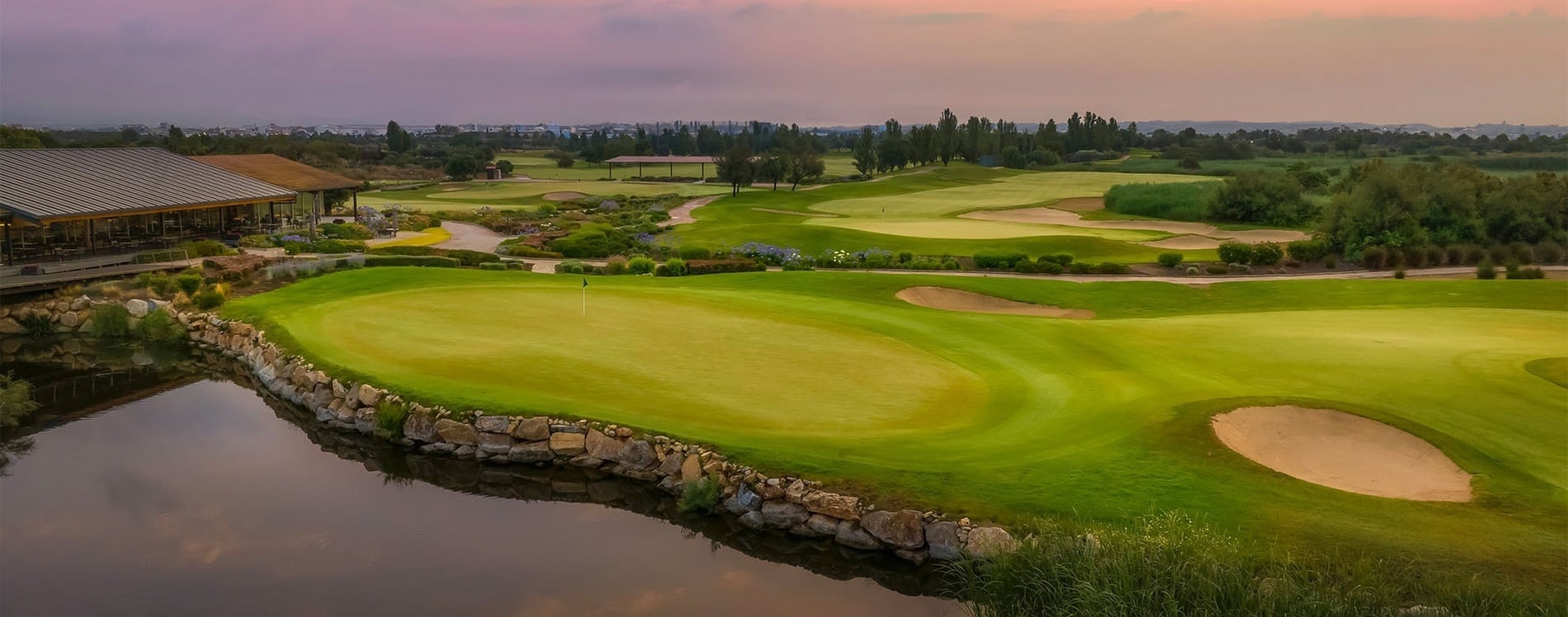 Ein Golfplatz mit mehreren Sandbunkern und saftig grünem Rasen erstreckt sich vor einem dichten Wald aus immergrünen Bäumen.