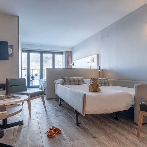 a teddy bear sits on a bed in a hotel room