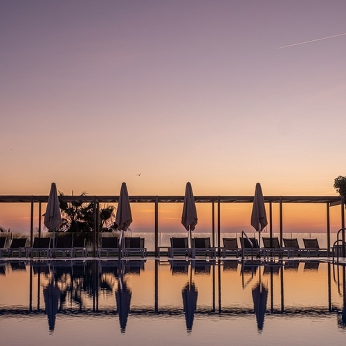 a swimming pool with chairs and umbrellas at sunset