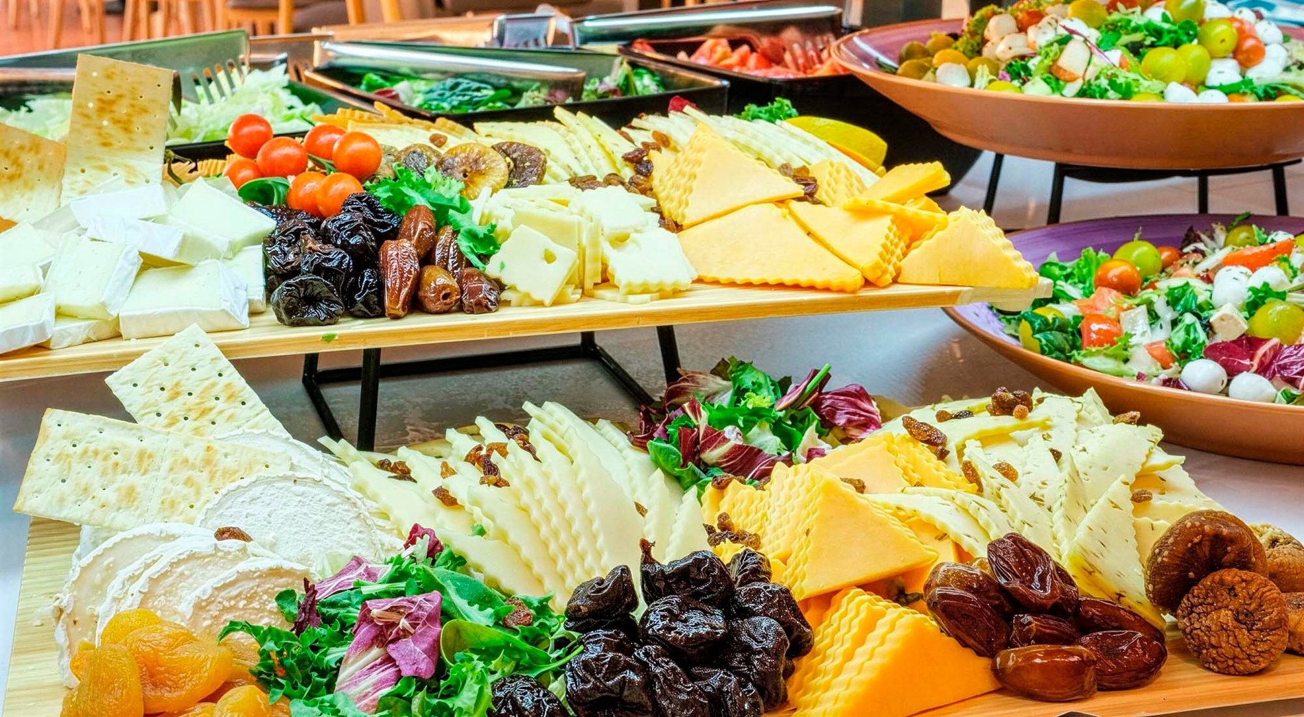 Un bufet abundant mostra diverses taules de formatges amb fruites seques i galetes salades, acompanyades d'amanides fresques.