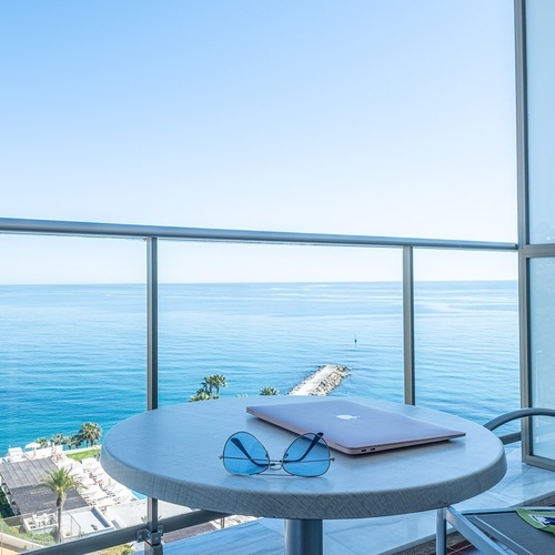 a laptop sits on a table on a balcony overlooking the ocean