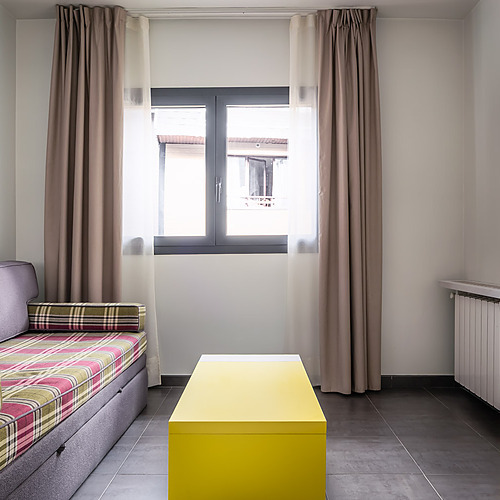 Modern hotel room with sofa, yellow desk, and TV. Hotel Cristina | Andorra | Estival Group | Official Web