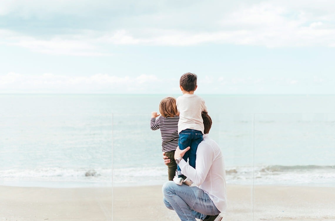 un homme porte deux enfants sur ses épaules sur la plage