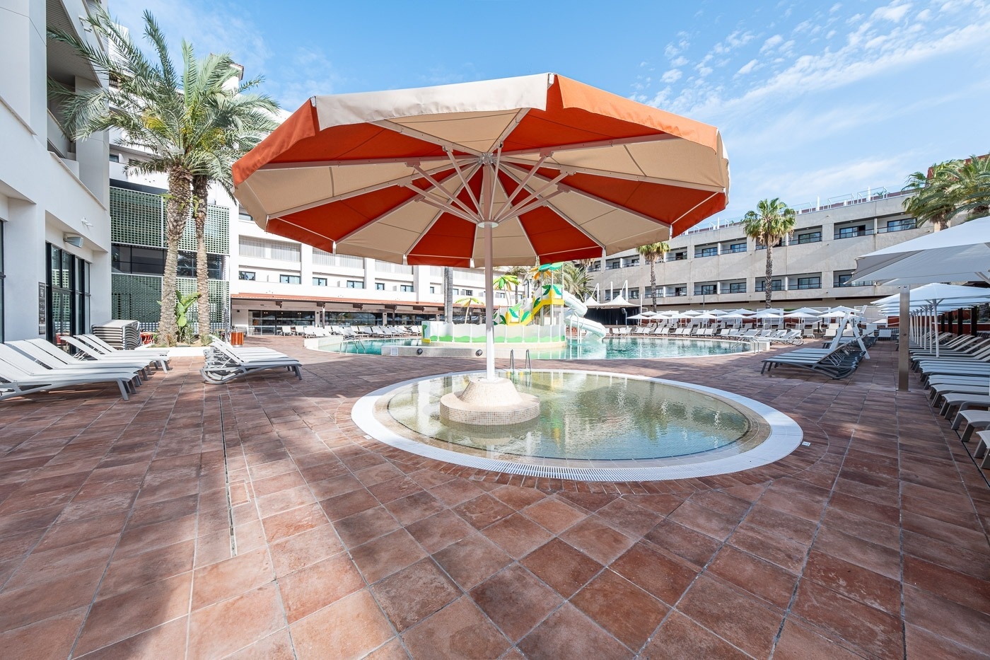a large orange and white umbrella is in the middle of a pool
