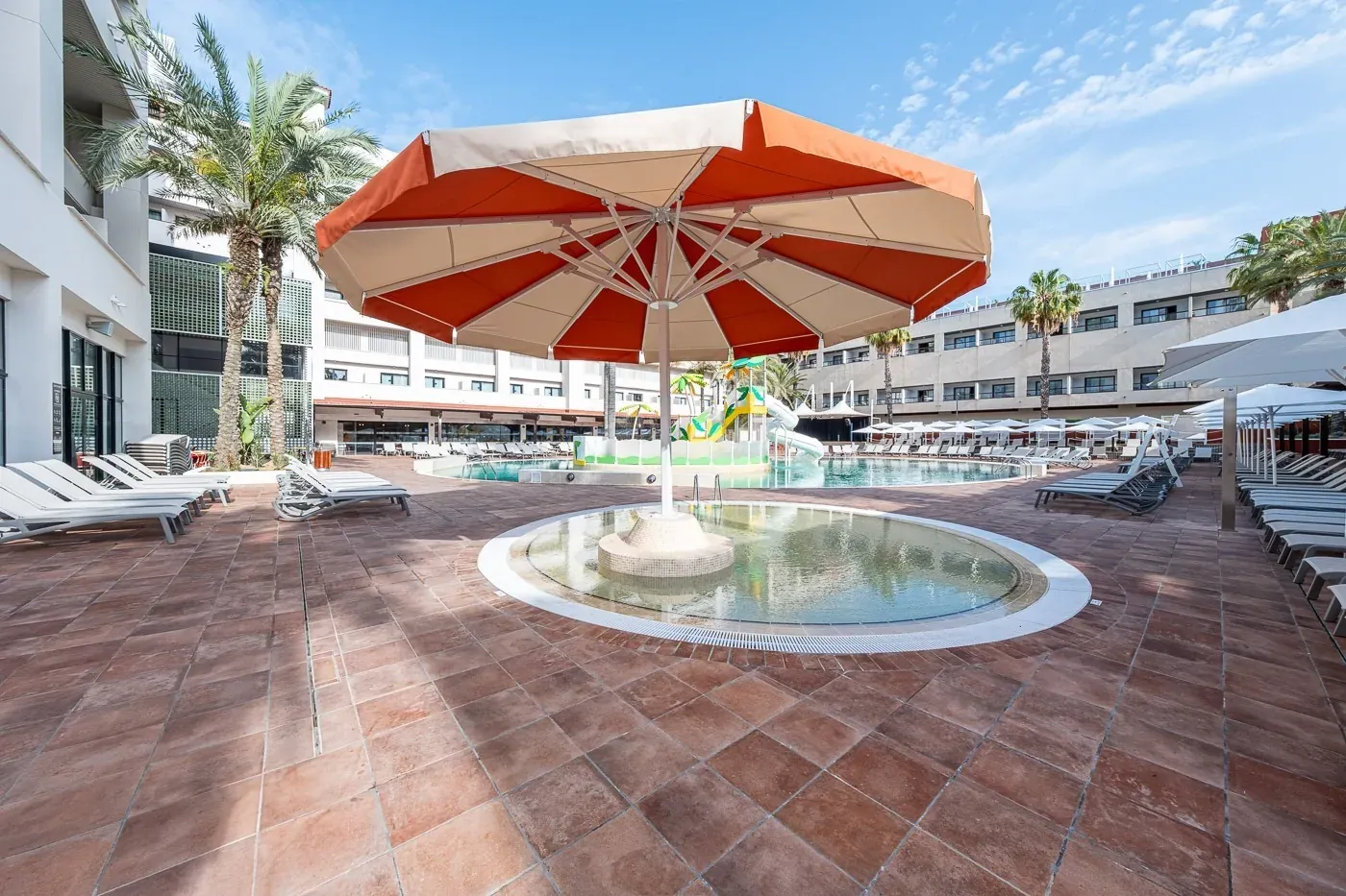 ESTIVAL: Corporate, pool, and sun loungers at hotel with palm trees.