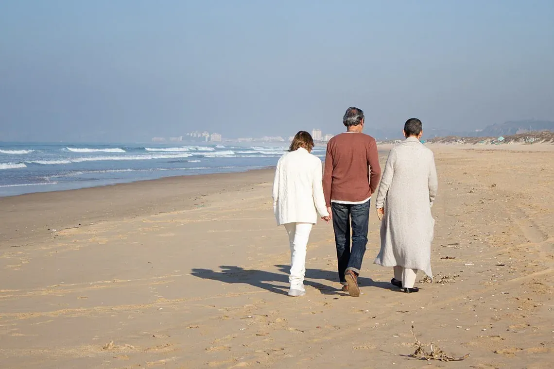 ESTIVAL Firmenveranstaltung: Paare spazieren am sonnigen Strand mit Meerblick.