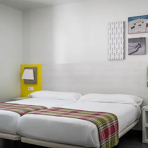 Modern twin hotel room withHotel Cristina | Andorra | Estival Group | Official Web, ski-themed art, and bedside table.