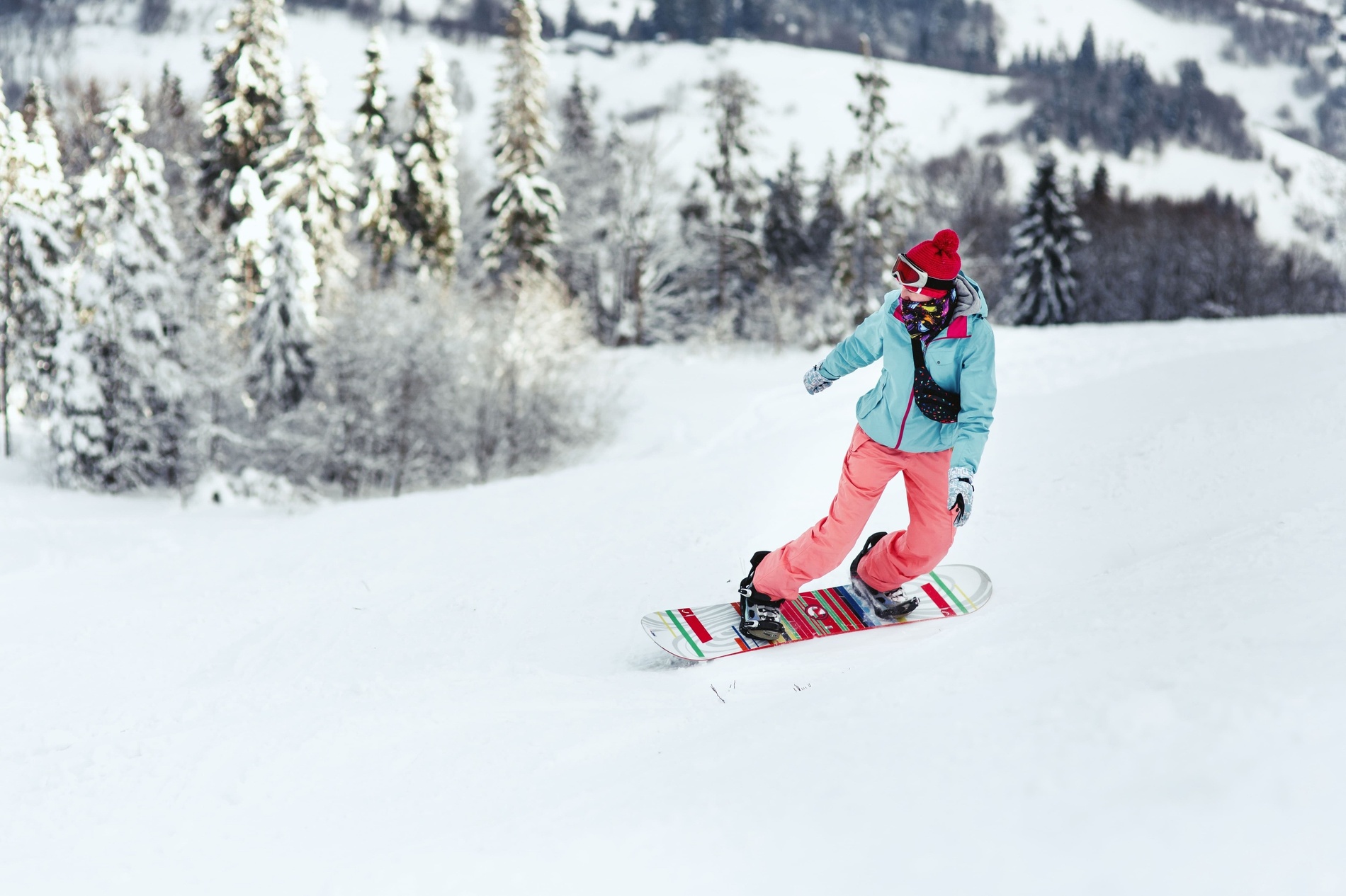 a snowboarder wearing a blue jacket and pink pants is riding down a snowy hill